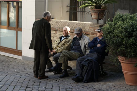 A group of elderly men chatting and relaxing on a bench in Grottammare, Italy, on a sunny day.