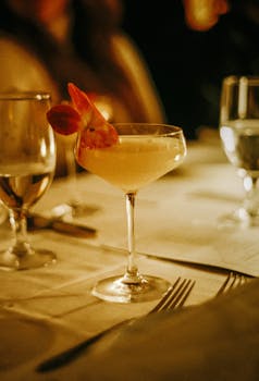 Sophisticated cocktail garnished with a flower on a dimly lit dining table setting.